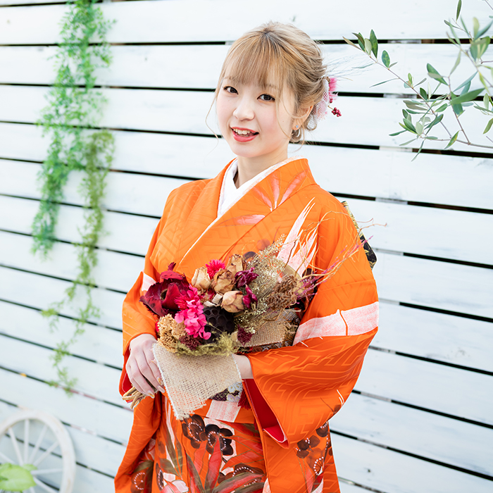 成人式で花束を持つオレンジ色の振袖を着た女性